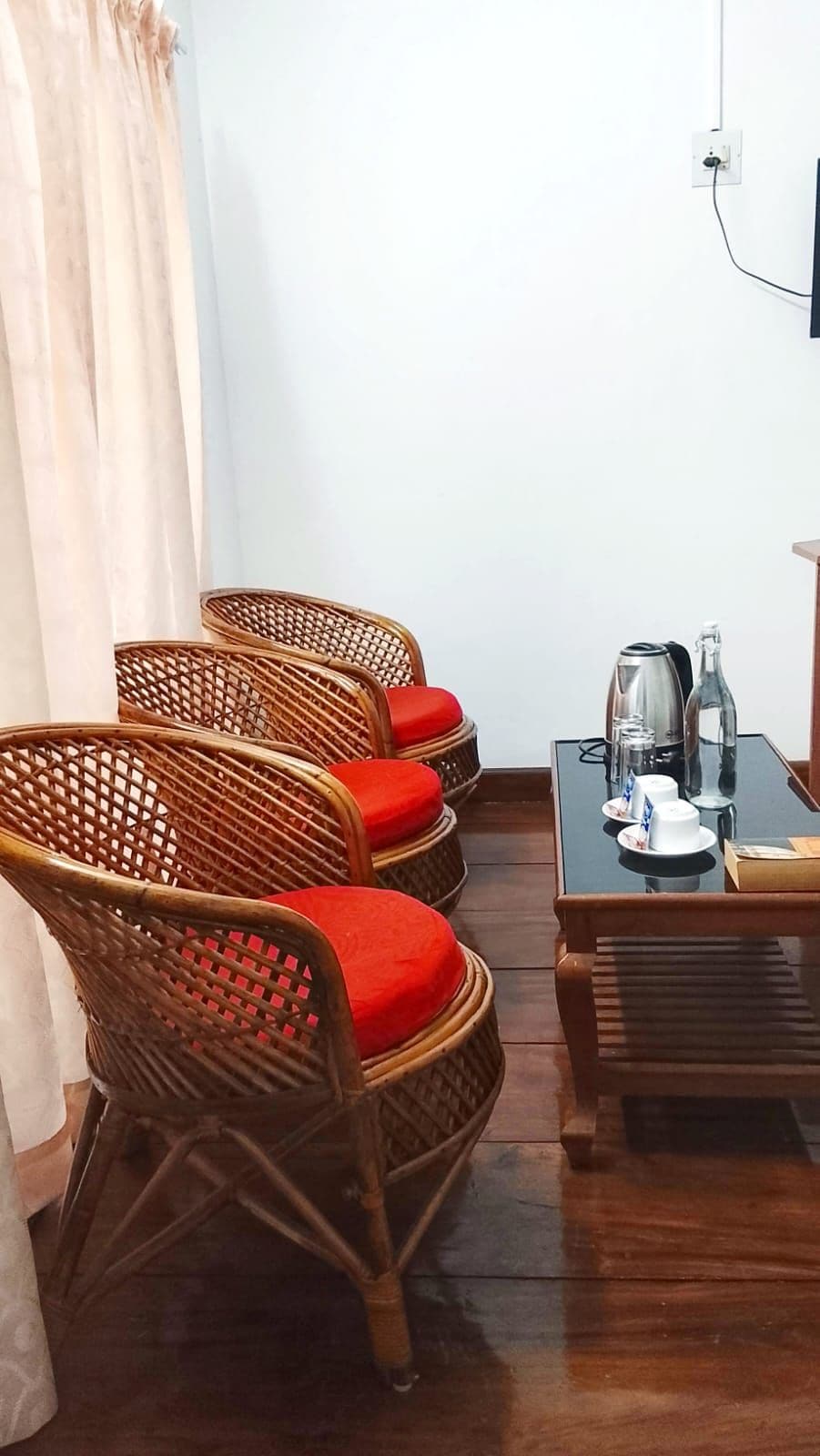 A corner room with wicker chairs, a table with a kettle, cups, and a bottle.