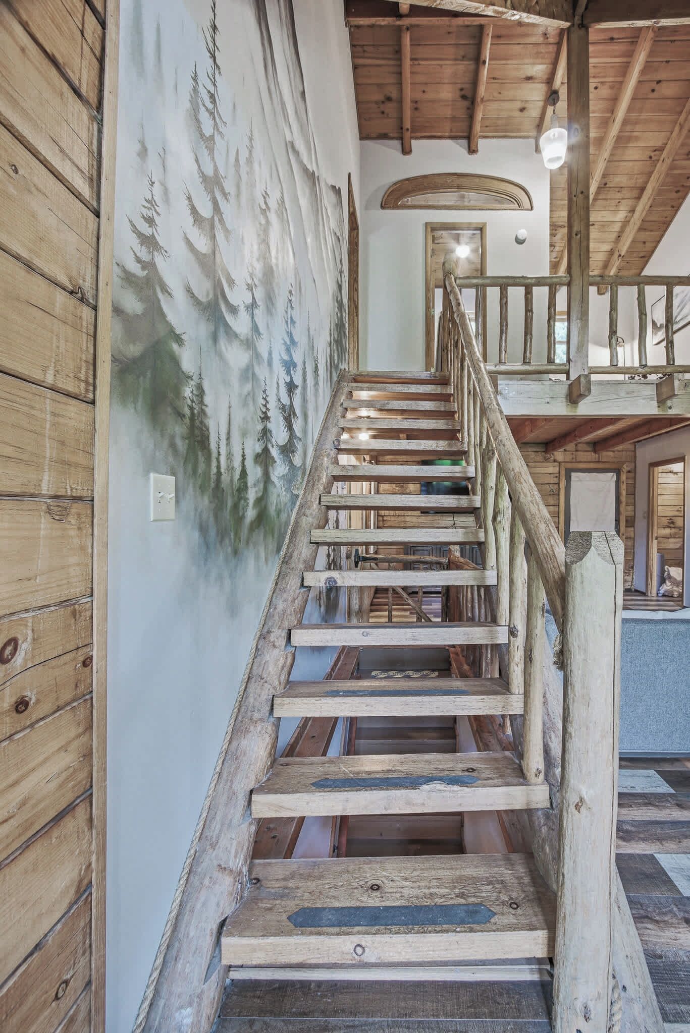 A wooden staircase with a railing, leading to a second-floor landing with a view of the outdoors.