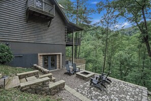Une cabane en rondins dotée d’un balcon, d’un escalier en pierre et d’un espace salon extérieur.