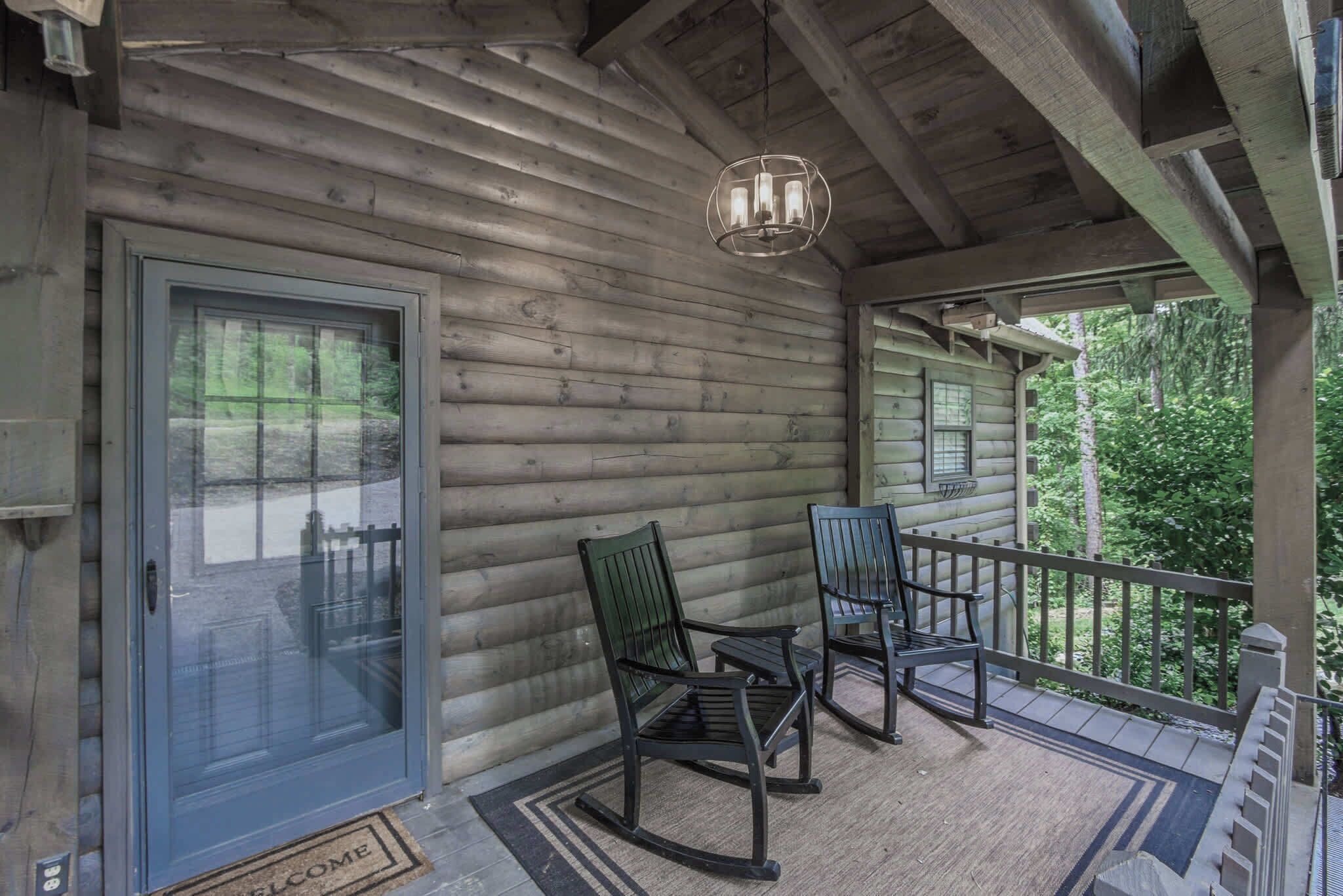 A log cabin with a porch, two rocking chairs, a door, and a welcome mat.