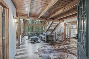 Un vaste espace de vie agrémenté d’un escalier, de poutres en bois et d’une grande fenêtre donnant sur un paysage verdoyant.