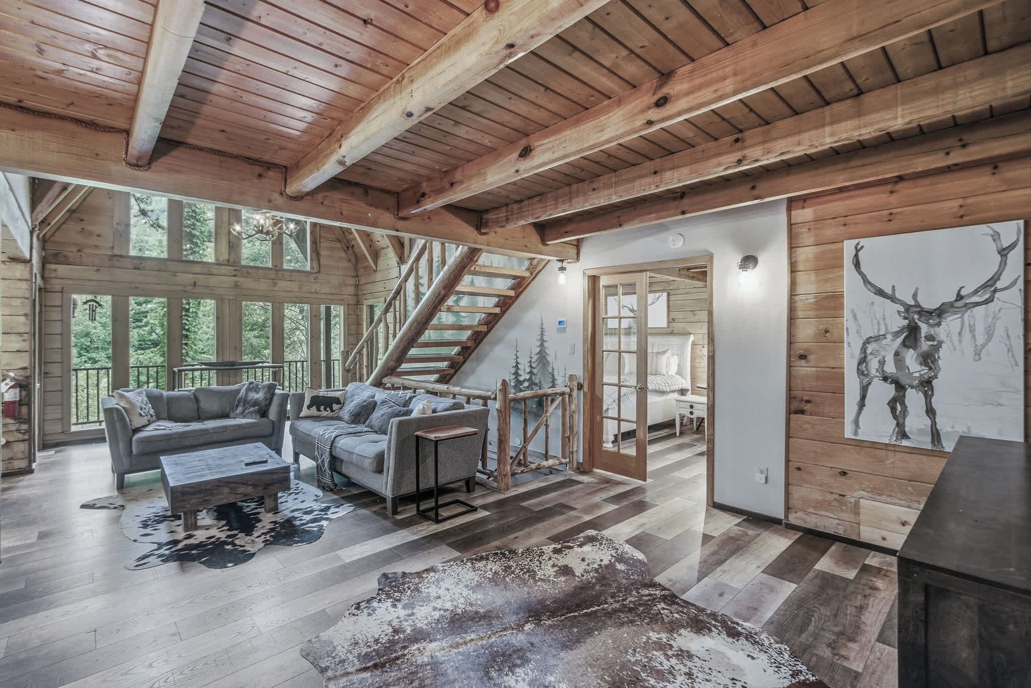 A spacious room with a wooden ceiling, a staircase, a sofa, a coffee table, and a large window.