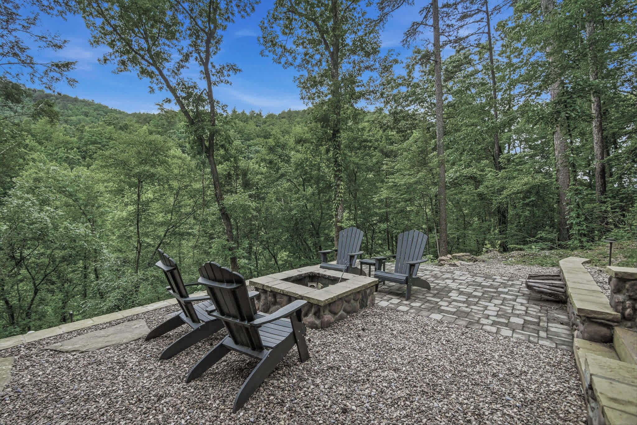 An outdoor seating area with Adirondack chairs and a fire pit surrounded by a stone wall.