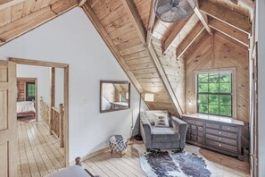 A loft bedroom with a sloped ceiling, a large window, a bed, a dresser, and a mirror. - Riverfront Retreat, Sleeps 10・Water Views・Hot Tub (Townsend)