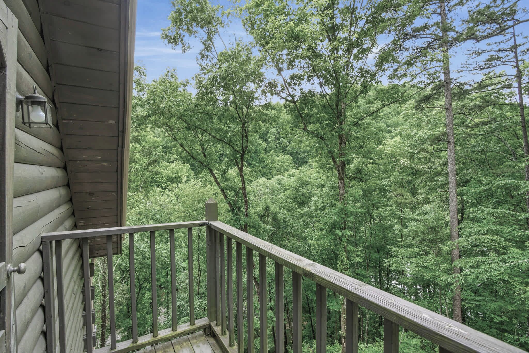 A wooden cabin with a balcony overlooking a dense forest.