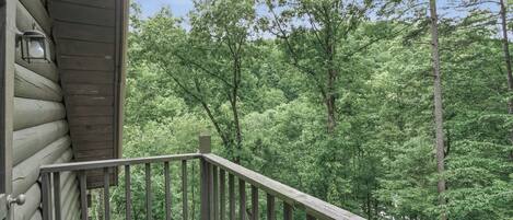 A wooden cabin with a balcony overlooking a dense forest.