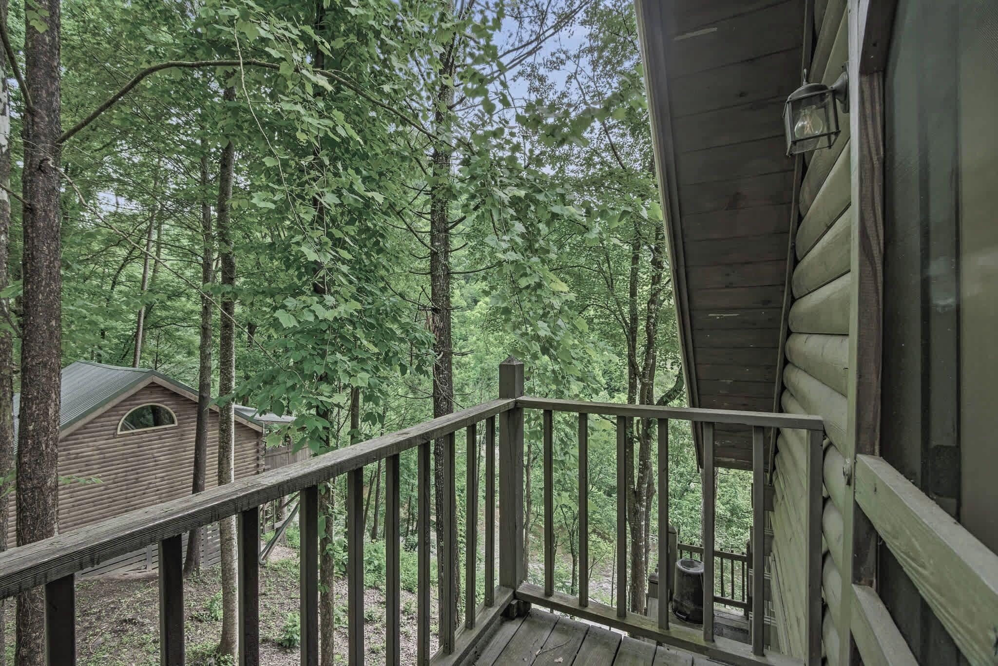 A wooden cabin with a balcony, surrounded by tall trees.