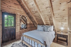 Une chambre dans une cabane en bois, avec un lit, une commode, un miroir et une porte.