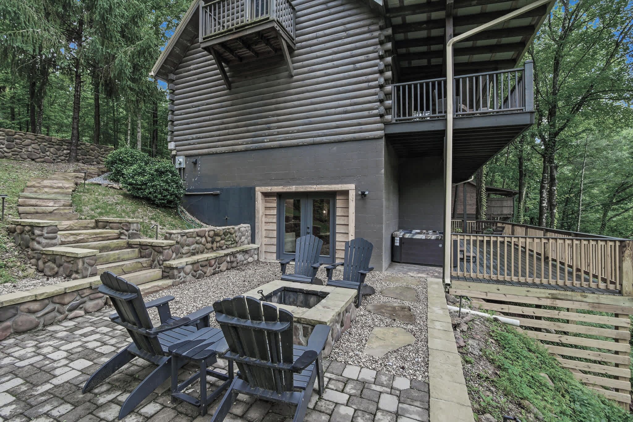 A log cabin with a stone fireplace, Adirondack chairs, and a stone staircase leading up to the entrance.
