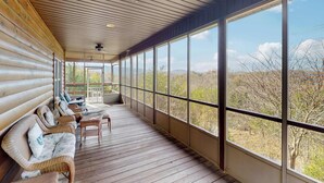 A log cabin with a covered porch, wicker furniture, and large windows offering a view of the surrounding landscape. - Peaceful Retreat, Sleeps 8・Near Douglas Lake・Grill (Dandridge)