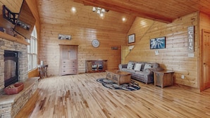 A spacious cabin interior with a stone fireplace, wooden floors, a sofa, and a television mounted on the wall. - Peaceful Retreat, Sleeps 8・Near Douglas Lake・Grill (Dandridge)