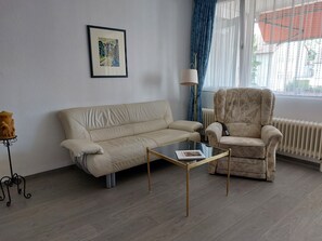 A living room with a sofa, armchair, glass coffee table, and a framed picture on the wall. - Apartment '58qm' with Balcony and Wi-Fi (Bad Krozingen)