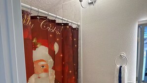 Ein Badezimmer mit einer weißen Toilette, einem Duschvorhang mit Weihnachtsmann-Motiv und einer Wandleuchte.