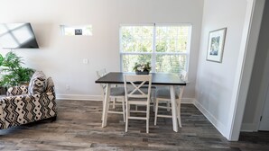 Un comedor con una mesa y sillas, un televisor montado en la pared, una ventana con persianas y una planta.