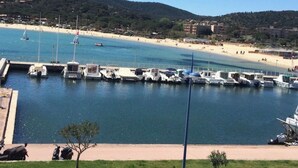 Uma marina com barcos atracados, uma praia e uma paisagem montanhosa ao fundo.