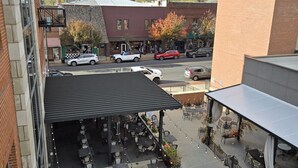 An outdoor patio area with tables and chairs, surrounded by buildings with brick facades and a mountain in the background. - Overlooks downtown Brevard with stunning mountain views! (Brevard)
