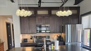 A modern kitchen with dark wood cabinets, stainless steel appliances, and a central island with bar stools. - Overlooks downtown Brevard with stunning mountain views! (Brevard)
