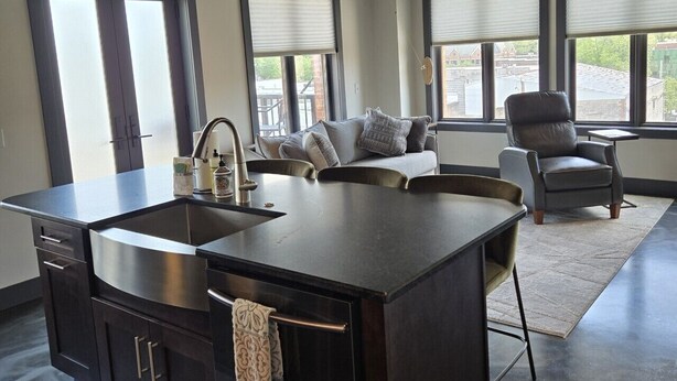 A modern kitchen with a central island, dark cabinetry, and a hanging light fixture. - Overlooks downtown Brevard with stunning mountain views! (Brevard)