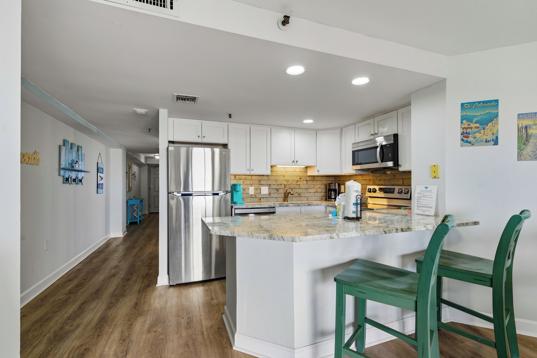 A modern kitchen with white cabinets, stainless steel appliances, and a marble countertop.