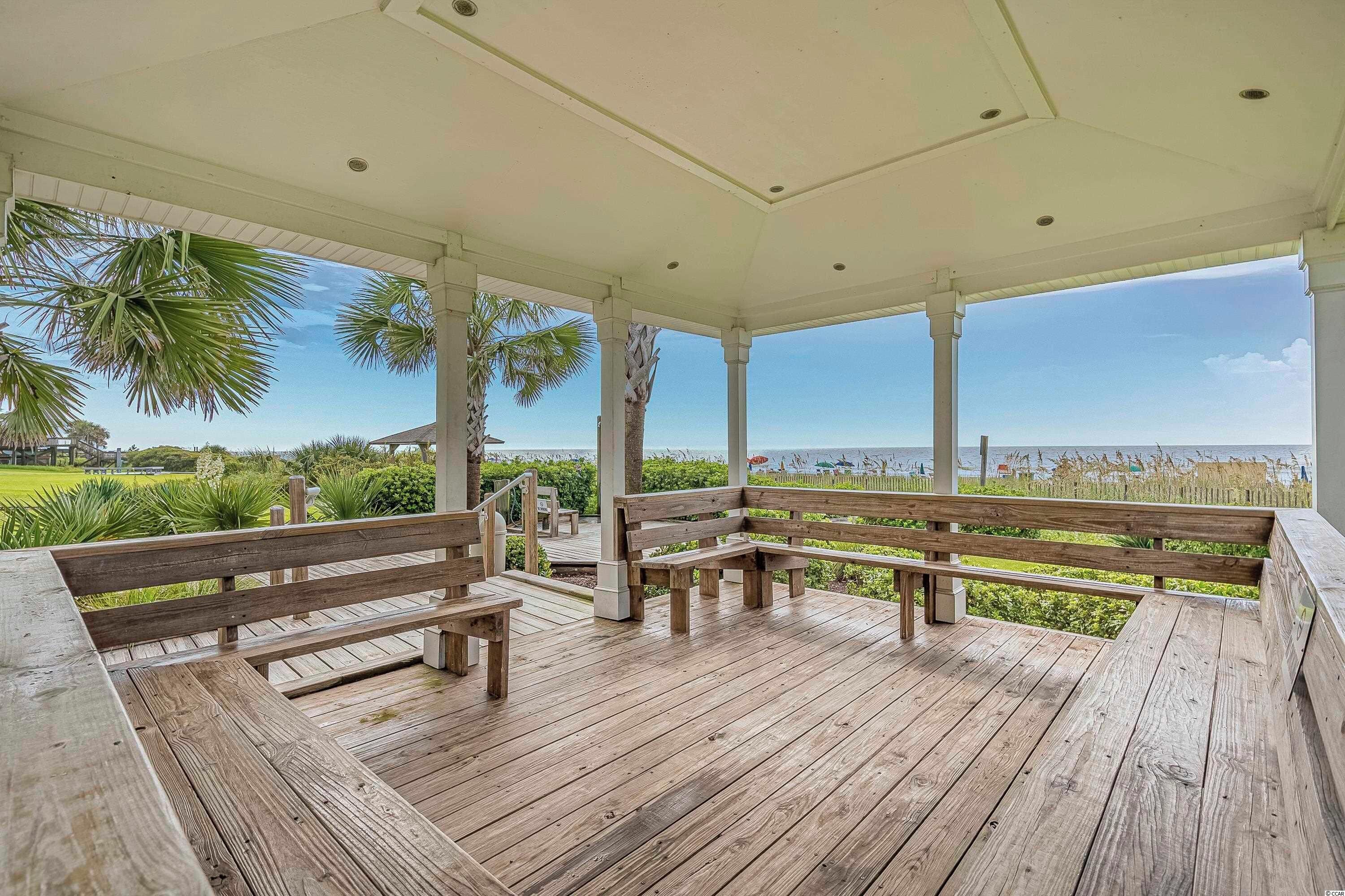 Una terrazza in legno coperta con panche, palme e vista sulla spiaggia.