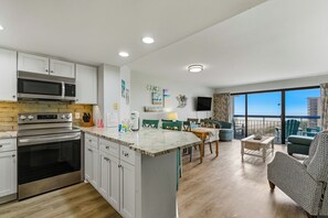 A modern kitchen with built-in appliances, a dining area with green chairs, and a balcony with a view. - 🌴Oceanfront with Stunning Views | Amazing Amenities | Forest Dunes 1001🌴 (Myrtle Beach)