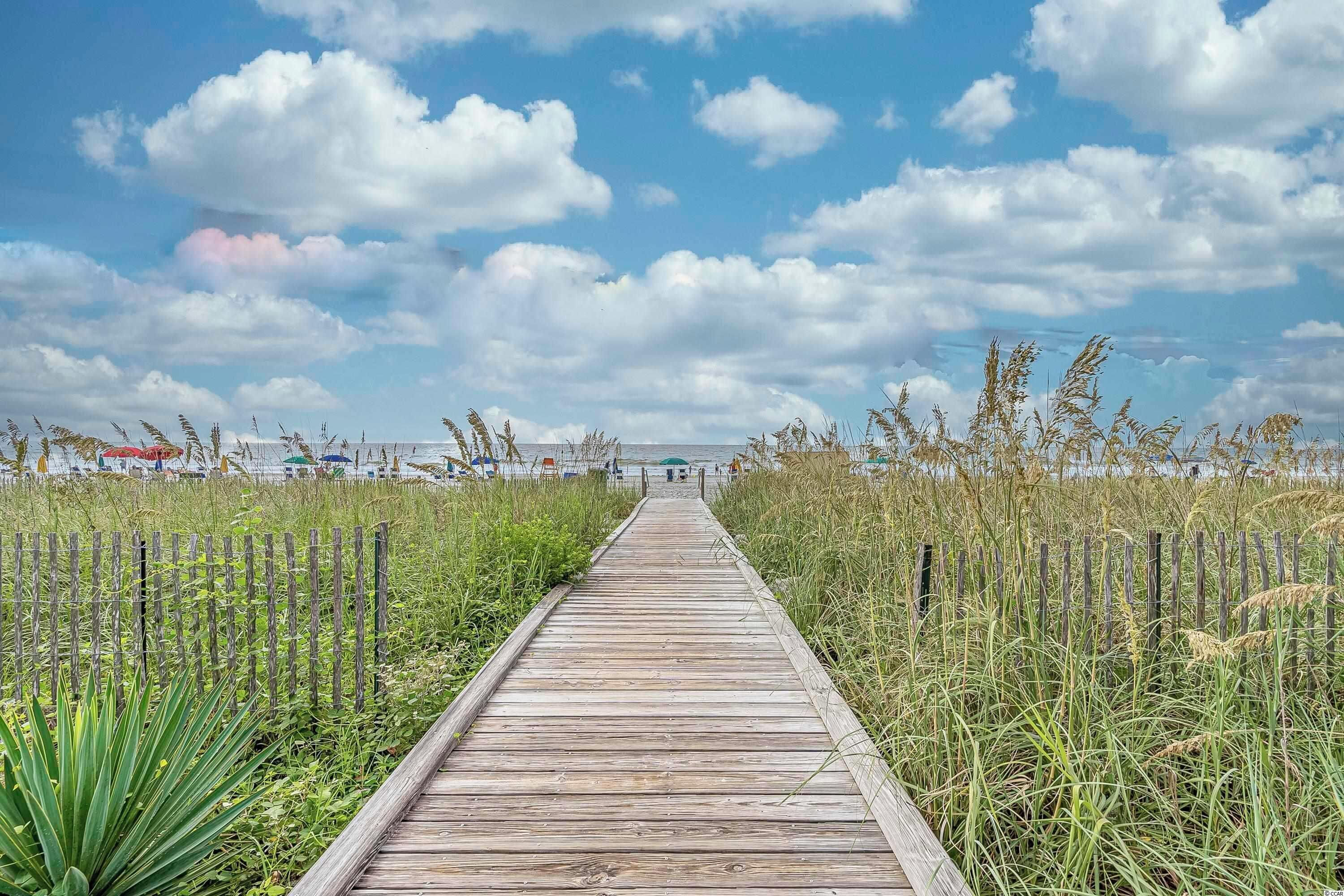 A wooden pathway leading through a grassy area with a wooden fence on both sides.