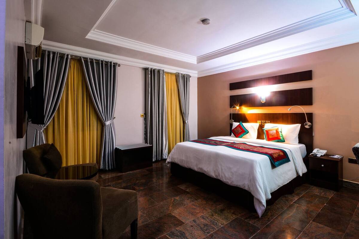 Une chambre d’hôtel avec un grand lit, une table de chevet, une chaise et une fenêtre avec des rideaux.