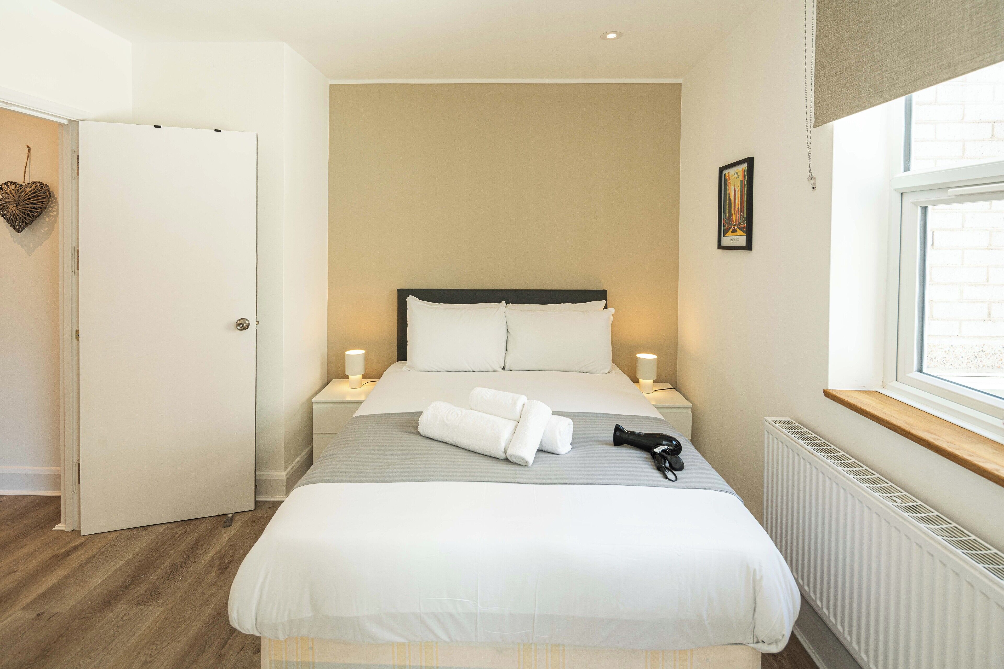 A neatly arranged bedroom with a large bed, bedside lamps, a radiator, and a window with a view.