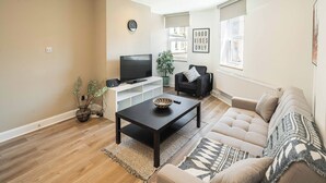 Ein modernes Wohnzimmer mit einer Couch, einem Couchtisch, einem Fernseher und einer Pflanze.