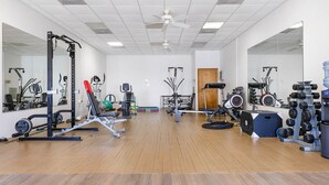 Uma academia com diversos equipamentos de exercício, piso de madeira e espelhos nas paredes.