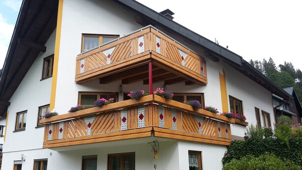 Un edificio de varios pisos con balcón de madera, ventanas y jardineras.