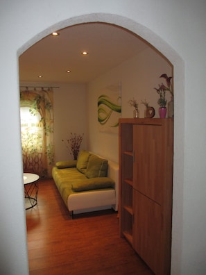 Un salon comprenant un canapé, un meuble en bois et un mur orné d’un motif abstrait vert.
