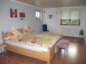 Une chambre à coucher avec un lit en bois, une literie à motifs floraux, une chaise, un radiateur et une fenêtre donnant sur un paysage agréable.