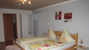Un dormitorio con una cama de madera, una mesita de noche pequeña, un taburete rosa y una puerta que da a otra habitación.