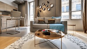 A modern living room with a sofa, coffee table, and a dining area with a chair and table. - JUST STEPS FROM THE ICONIC CHAMPS-ÉLYSÉES - SLEEPS 12 -  RUE LA BOÉTIE (Paris)