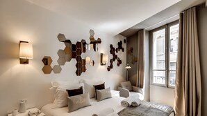 A modern hotel room with a large bed, bedside tables, a wall-mounted light fixture, and a window with curtains. - JUST STEPS FROM THE ICONIC CHAMPS-ÉLYSÉES - SLEEPS 12 -  RUE LA BOÉTIE (Paris)