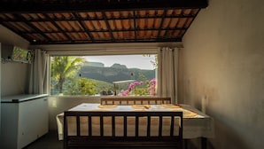 A room with a table and chairs, a window with a view of greenery and mountains, and a tiled ceiling. - Casa de Campo Para so da Serra com Piscina e Vista (Iramaia)