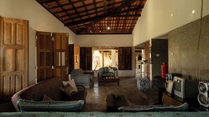 A spacious living room with a high ceiling, wooden doors, and a mix of seating including a sofa and armchairs. - Casa de Campo Para so da Serra com Piscina e Vista (Iramaia)