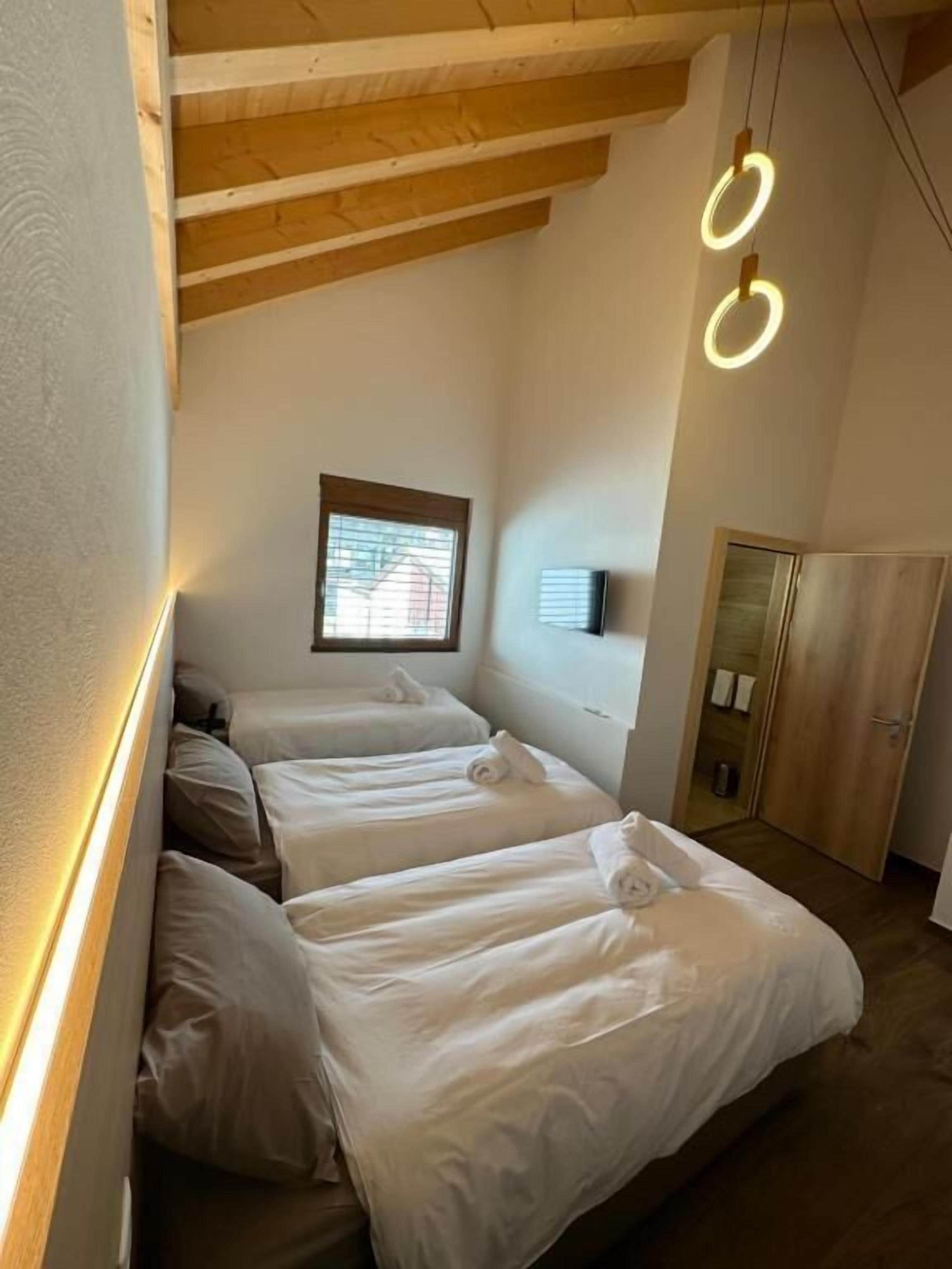 Una habitación con tres camas, vigas de madera en el techo y un ventanal pequeño.