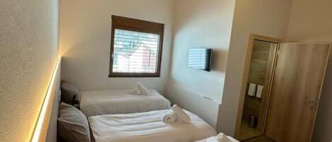 Una habitación con tres camas, vigas de madera en el techo y un ventanal pequeño.