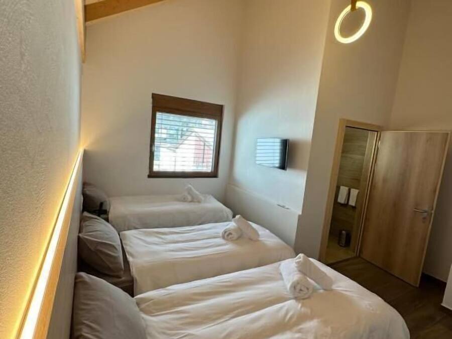 A room with three beds, wooden beams on the ceiling, and a small window.