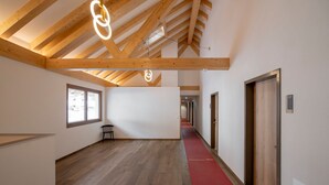 Un pasillo espacioso con vigas de madera, alfombra roja y vista a un coche a través de una ventana.
