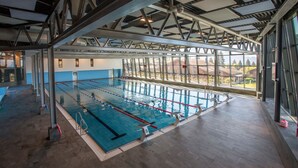 Una piscina cubierta con carriles delimitados, un techo alto con vigas metálicas y ventanas amplias que ofrecen vistas al exterior.