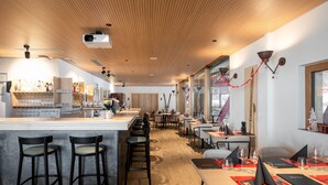 Un restaurante moderno con zona de bar, techo de madera y grandes ventanales.