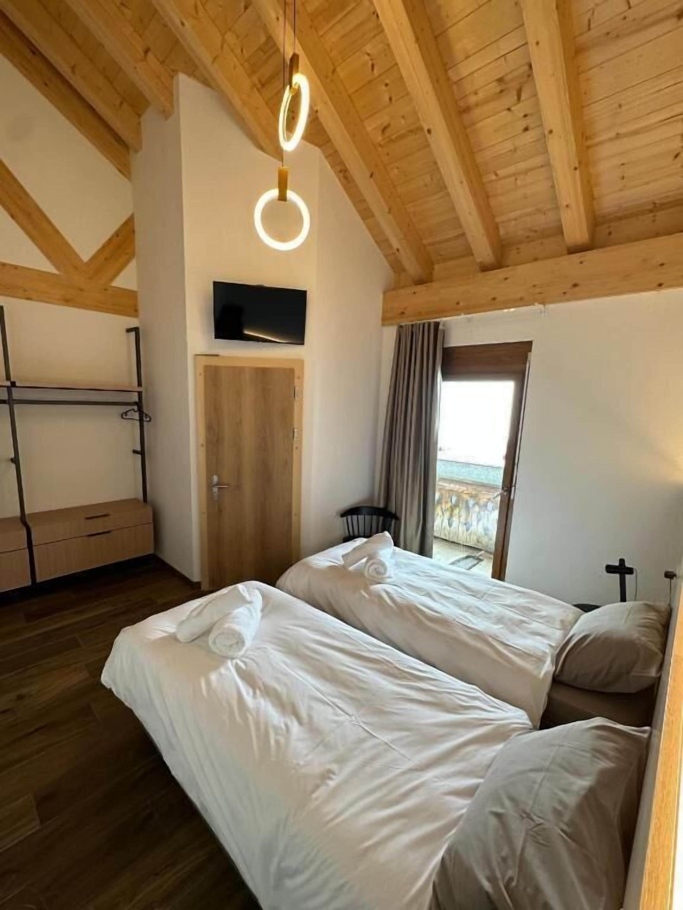 Ein Schlafzimmer mit zwei Betten, Holzbalken, einem Fernseher und Blick ins Freie.