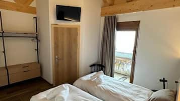 Ein Schlafzimmer mit zwei Betten, Holzbalken, einem Fernseher und Blick ins Freie.
