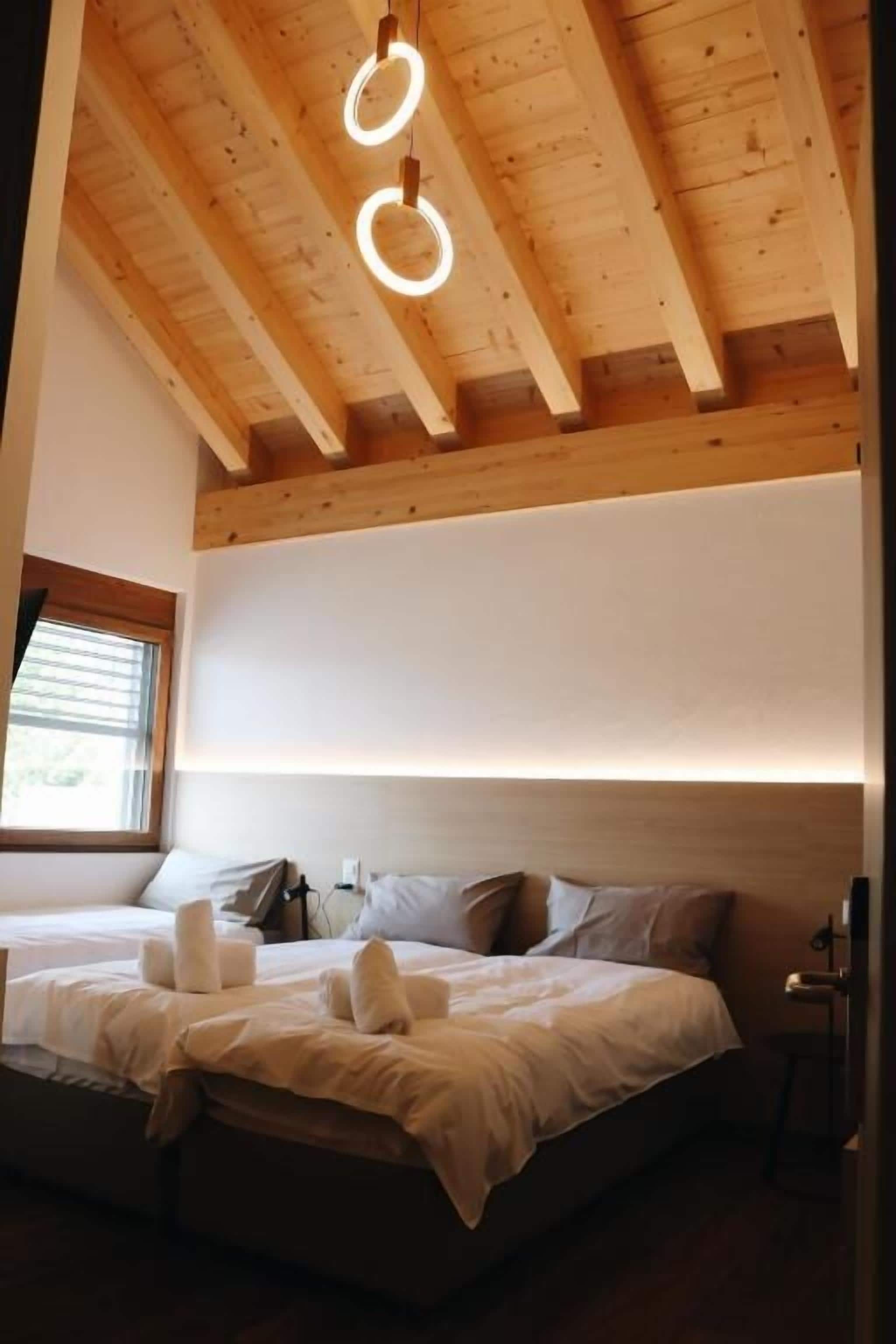 A bedroom with a wooden ceiling, a bed with white bedding, and a window with blinds.
