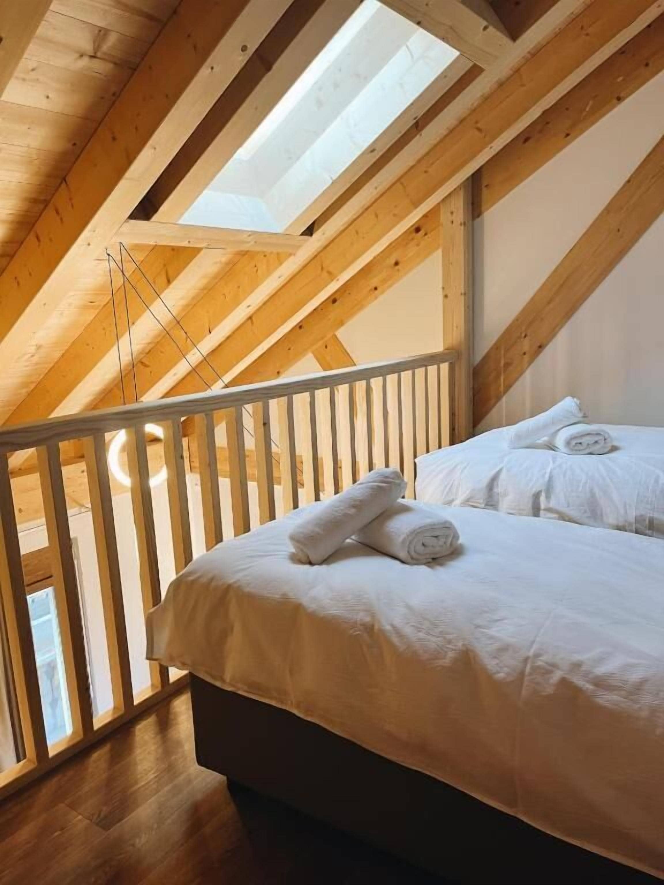 Une chambre avec un puits de lumière, des poutres en bois et un lit recouvert de draps blancs.