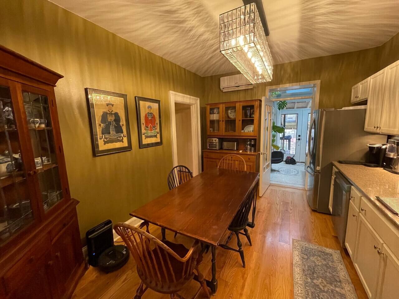 A dining area with a wooden table and chairs, a cabinet with glass doors, and a chandelier.