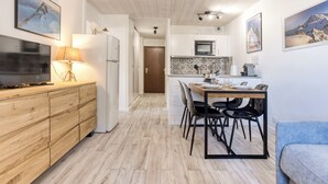 Een moderne keuken met houten kastjes, een eettafel met stoelen, een televisie en een koelkast.